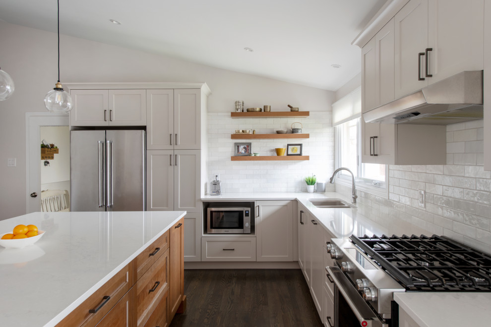 Open concept kitchen - mid-sized transitional l-shaped medium tone wood floor, gray floor and vaulted ceiling open concept kitchen idea in Ottawa with a double-bowl sink, shaker cabinets, gray cabinets, quartz countertops, white backsplash, subway tile backsplash, stainless steel appliances, an island and white countertops