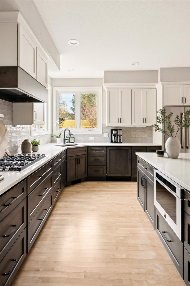 Example of a large transitional u-shaped light wood floor and brown floor open concept kitchen design in Denver with an undermount sink, shaker cabinets, granite countertops, beige backsplash, porcelain backsplash, stainless steel appliances, an island and white countertops