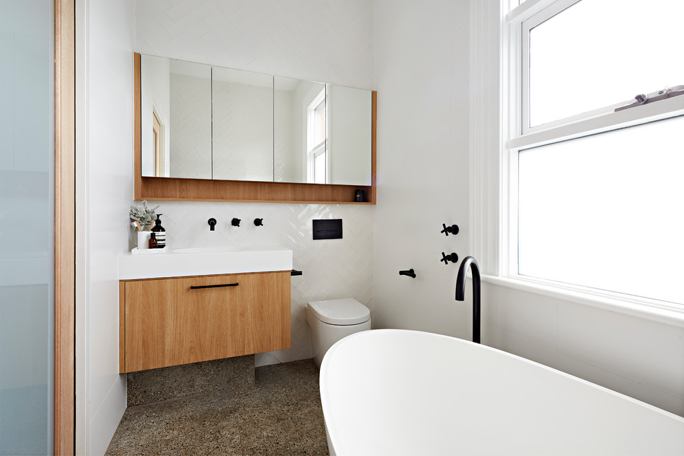 This is an example of a small contemporary 3/4 bathroom in Melbourne with light wood cabinets, a freestanding tub, an open shower, a wall-mount toilet, white tile, white walls, terrazzo floors, an undermount sink, multi-coloured floor, an open shower, white benchtops, furniture-like cabinets, subway tile and engineered quartz benchtops.