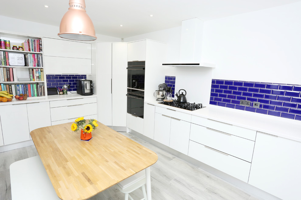 Photo of a mid-sized contemporary u-shaped separate kitchen in Other with an integrated sink, flat-panel cabinets, white cabinets, solid surface benchtops, blue splashback, ceramic splashback, black appliances and white benchtop.