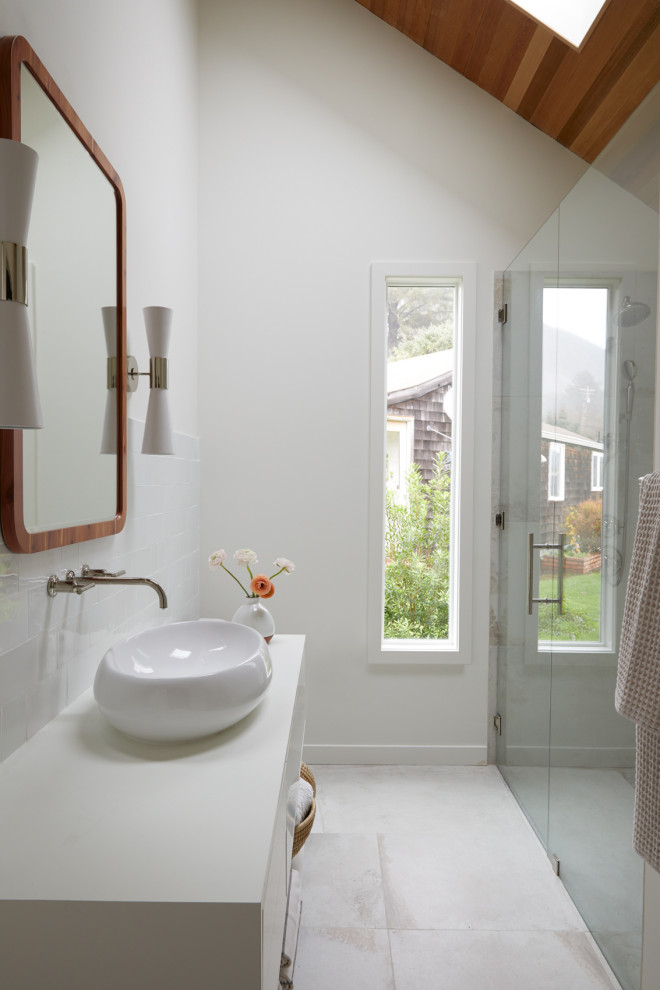 Photo of a mid-sized beach style master bathroom in Other with flat-panel cabinets, white cabinets, a curbless shower, a one-piece toilet, white tile, ceramic tile, white walls, porcelain floors, a vessel sink, multi-coloured floor, a hinged shower door, white benchtops, a shower seat, a single vanity, a floating vanity and vaulted.