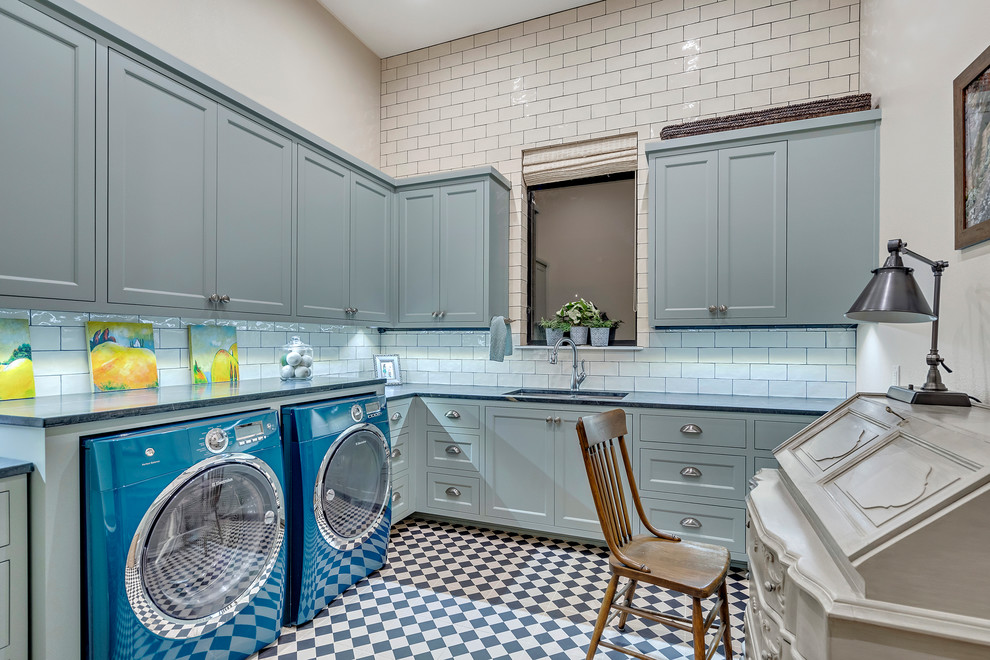 Photo of a large mediterranean u-shaped utility room in Austin with an undermount sink, shaker cabinets, blue cabinets, soapstone benchtops, beige walls, ceramic floors, a side-by-side washer and dryer, multi-coloured floor and grey benchtop.