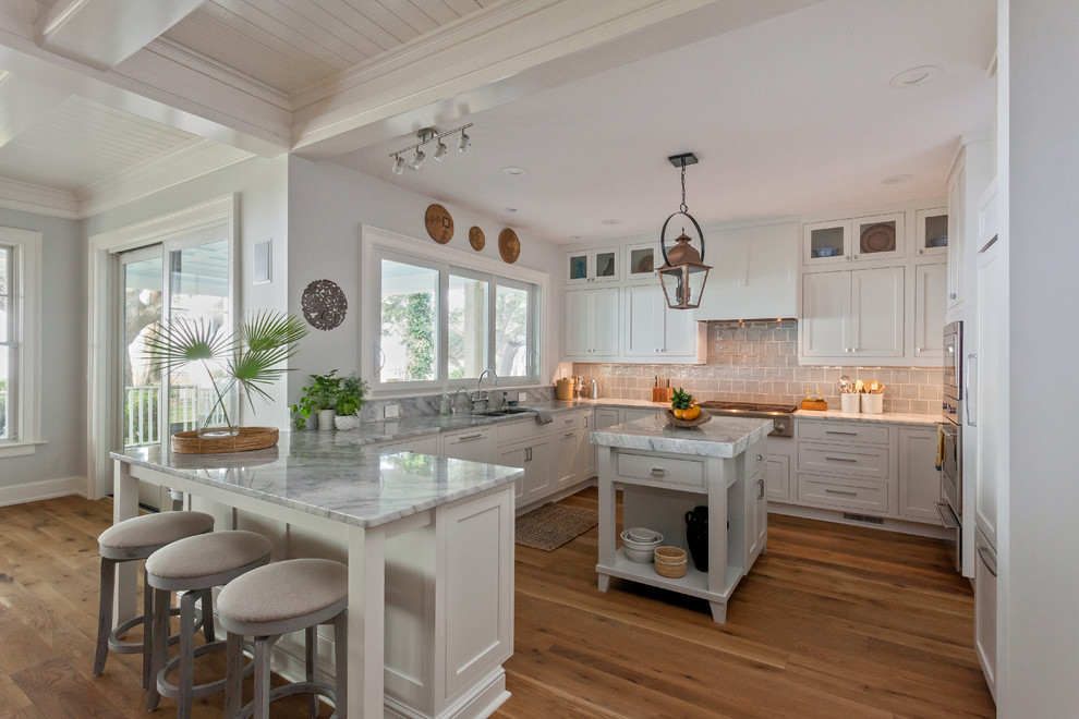 This is an example of a traditional u-shaped kitchen in Charleston with shaker cabinets, white cabinets, grey splashback, stainless steel appliances, medium hardwood floors and with island.