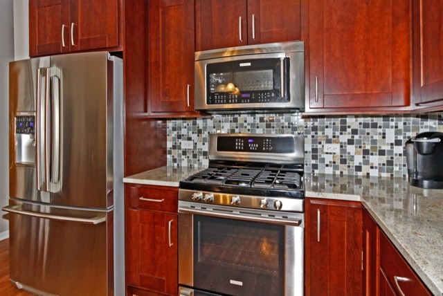 Example of a mid-sized transitional l-shaped medium tone wood floor eat-in kitchen design in Chicago with an undermount sink, recessed-panel cabinets, medium tone wood cabinets, granite countertops, gray backsplash, glass tile backsplash, stainless steel appliances, gray walls and an island