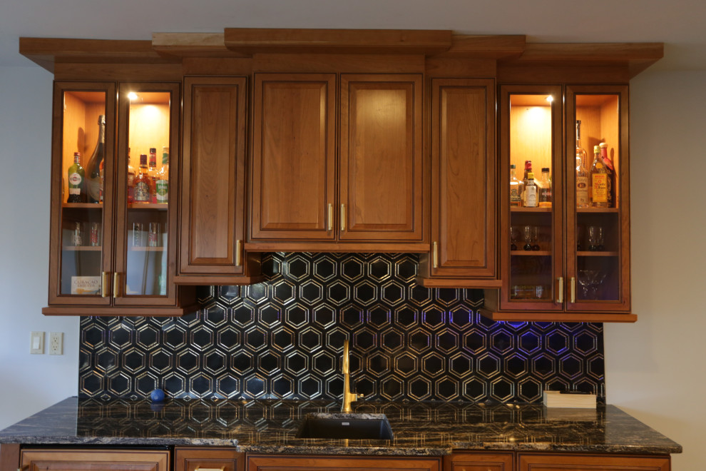Photo of a mid-sized traditional single-wall wet bar in Baltimore with an undermount sink, raised-panel cabinets, medium wood cabinets, granite benchtops, black splashback, marble splashback, plywood floors, beige floor and black benchtop.