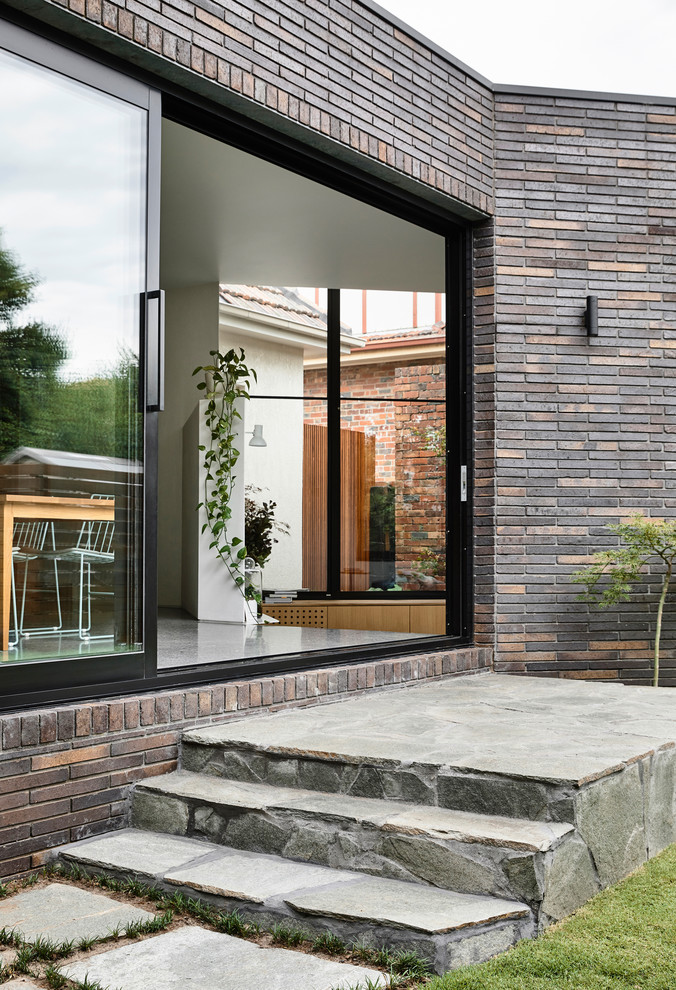 Photo of a mid-sized contemporary two-storey brick brown house exterior in Melbourne with a flat roof and a metal roof.