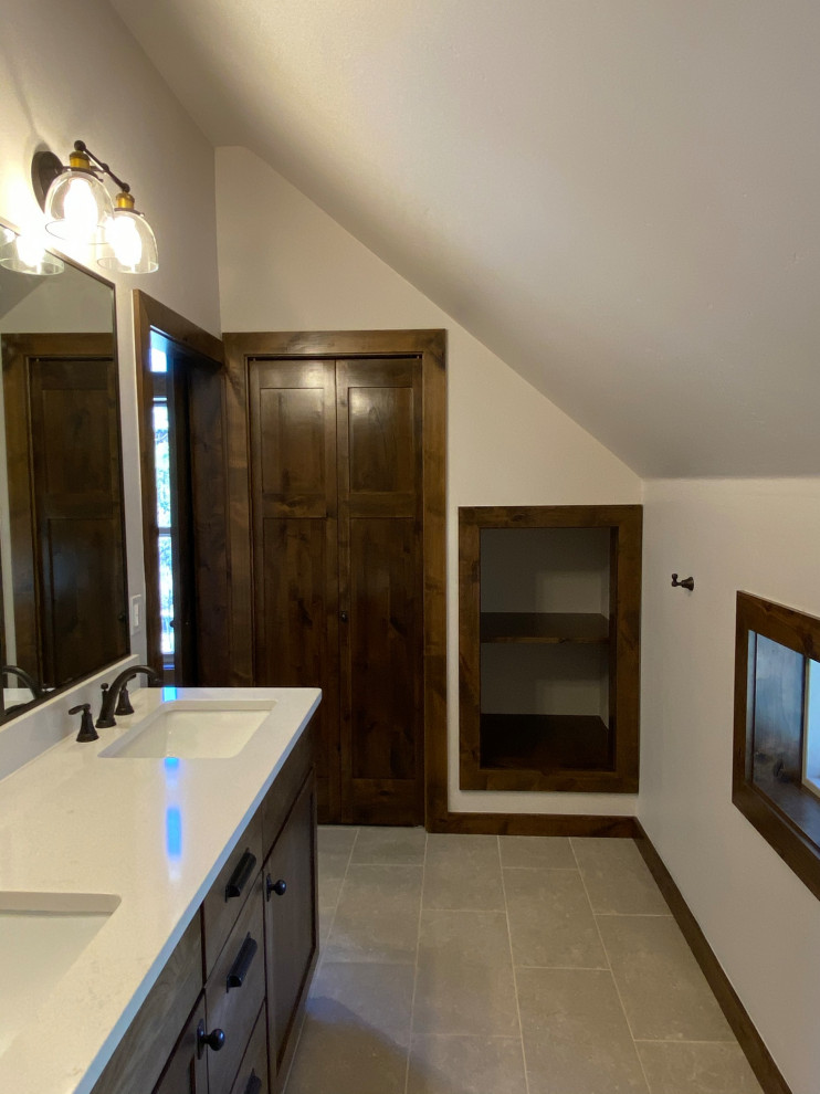 Example of a mountain style limestone floor and double-sink bathroom design with shaker cabinets, brown cabinets, quartzite countertops, white countertops, a built-in vanity, an undermount sink and a niche