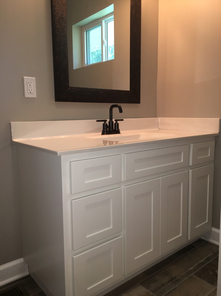 Example of a mid-sized transitional 3/4 porcelain tile and brown floor alcove shower design with shaker cabinets, white cabinets, gray walls, an integrated sink, solid surface countertops and a hinged shower door