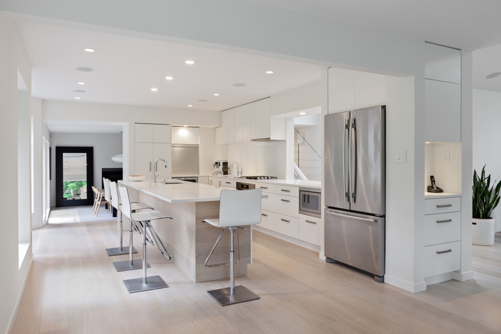 Contemporary u-shaped eat-in kitchen in Vancouver with an undermount sink, flat-panel cabinets, white cabinets, white splashback, stainless steel appliances, light hardwood floors and with island.