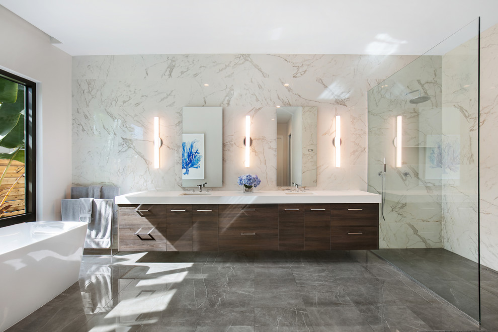 Large modern master bathroom in Tampa with flat-panel cabinets, dark wood cabinets, a freestanding tub, a curbless shower, a two-piece toilet, white tile, porcelain tile, white walls, porcelain floors, an undermount sink, engineered quartz benchtops, grey floor, an open shower and white benchtops.
