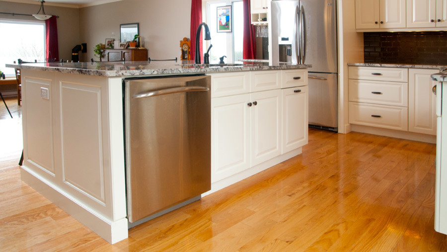 Example of a mid-sized transitional l-shaped light wood floor eat-in kitchen design with an undermount sink, raised-panel cabinets, white cabinets, granite countertops, gray backsplash, glass tile backsplash, stainless steel appliances and an island