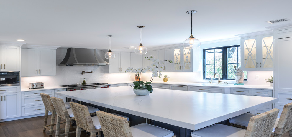 Large modern l-shaped eat-in kitchen in New York with an undermount sink, recessed-panel cabinets, white cabinets, quartz benchtops, white splashback, stainless steel appliances, medium hardwood floors, with island, brown floor and white benchtop.