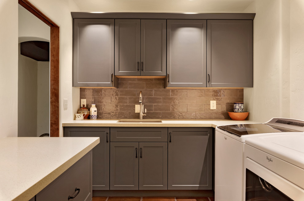 Inspiration for a mid-sized l-shaped dedicated laundry room in Phoenix with an undermount sink, shaker cabinets, grey cabinets, white walls, terra-cotta floors, a side-by-side washer and dryer, brown floor and white benchtop.