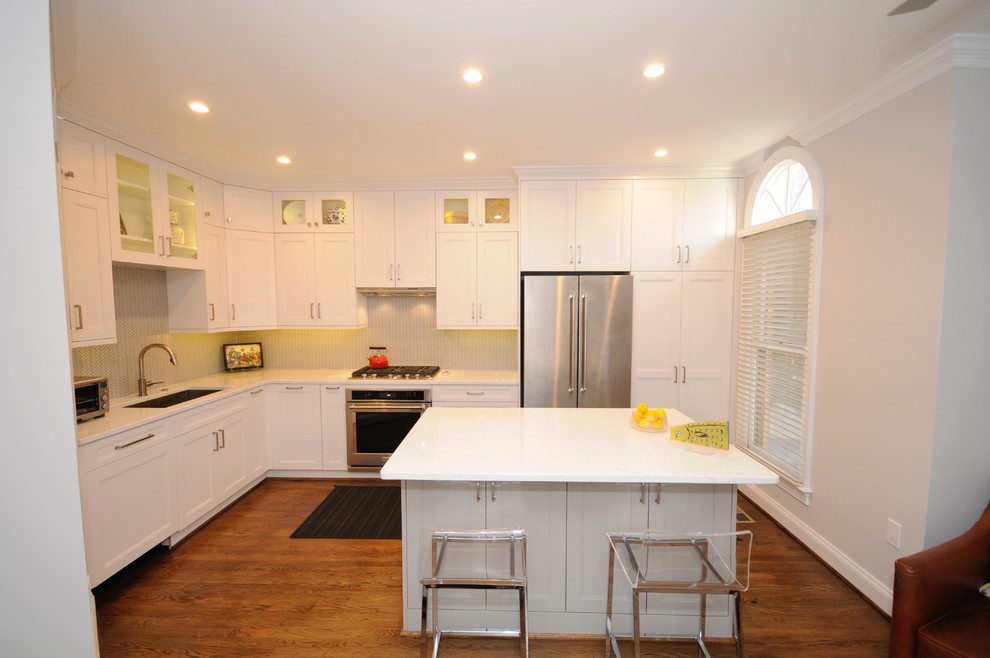 Eat-in kitchen - mid-sized transitional l-shaped medium tone wood floor eat-in kitchen idea in DC Metro with a single-bowl sink, recessed-panel cabinets, white cabinets, quartz countertops, white backsplash, mosaic tile backsplash, stainless steel appliances and an island
