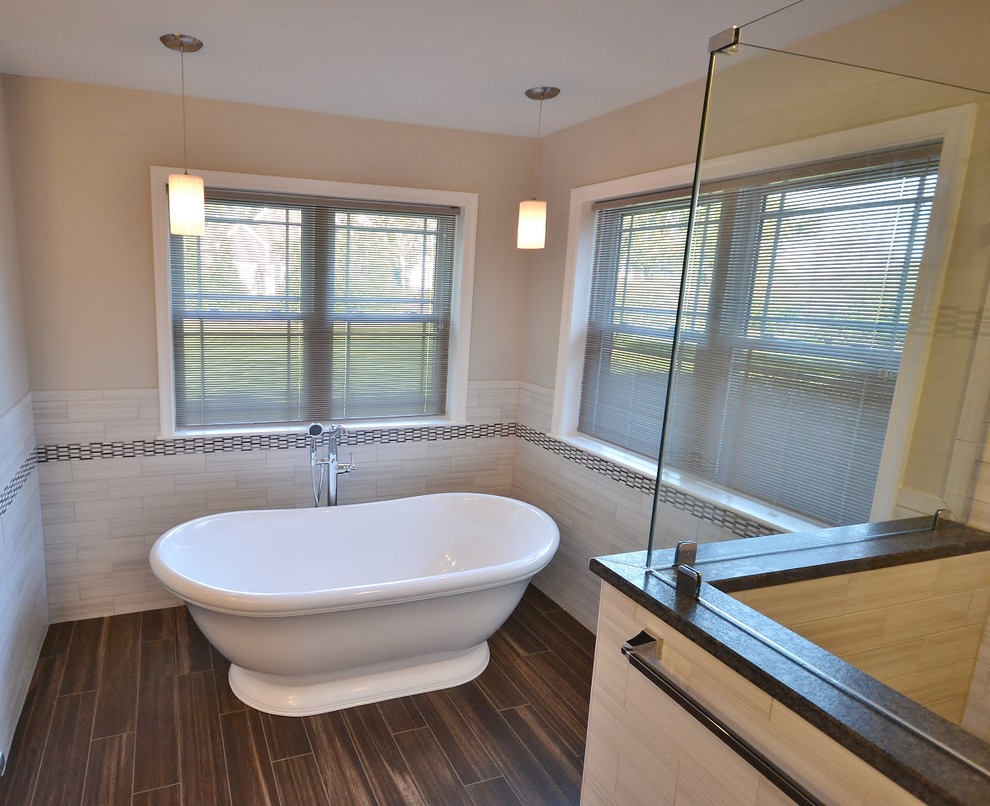 This is an example of a large transitional master bathroom in Philadelphia with recessed-panel cabinets, white cabinets, a freestanding tub, a double shower, a one-piece toilet, beige tile, subway tile, beige walls, dark hardwood floors, an undermount sink, granite benchtops, brown floor and a hinged shower door.