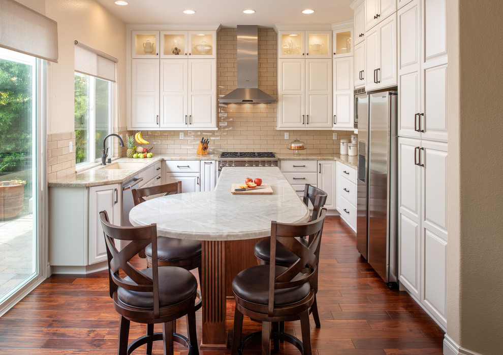 Design ideas for a traditional u-shaped kitchen in San Diego with an undermount sink, raised-panel cabinets, white cabinets, beige splashback, subway tile splashback, stainless steel appliances, medium hardwood floors, with island and beige benchtop.
