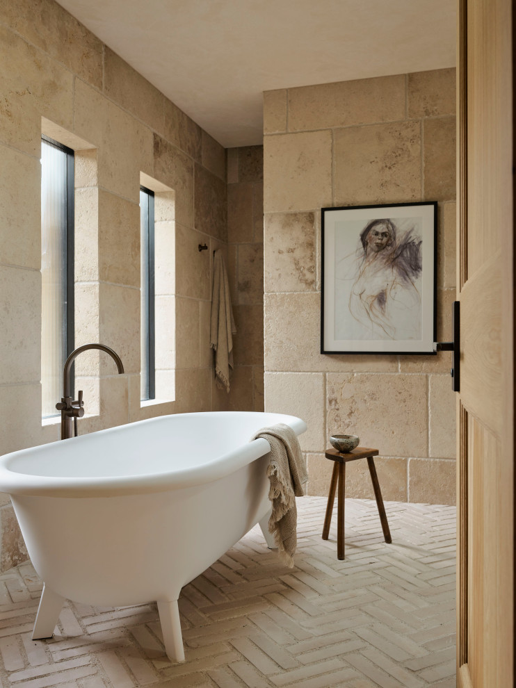 This is an example of an expansive traditional ensuite bathroom in Sydney with a built in vanity unit, a freestanding bath, beige tiles, beige walls, brick flooring and white floors.