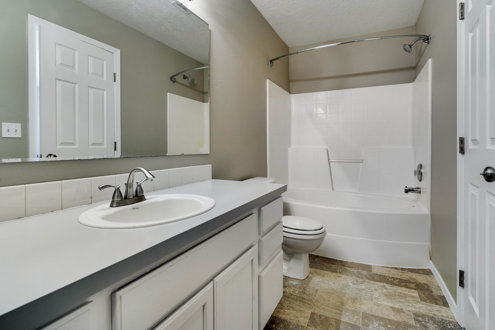 Photo of a small traditional master bathroom in Boise with raised-panel cabinets, white cabinets, an alcove tub, a shower/bathtub combo, a two-piece toilet, white tile, porcelain tile, beige walls, vinyl floors, a drop-in sink and laminate benchtops.