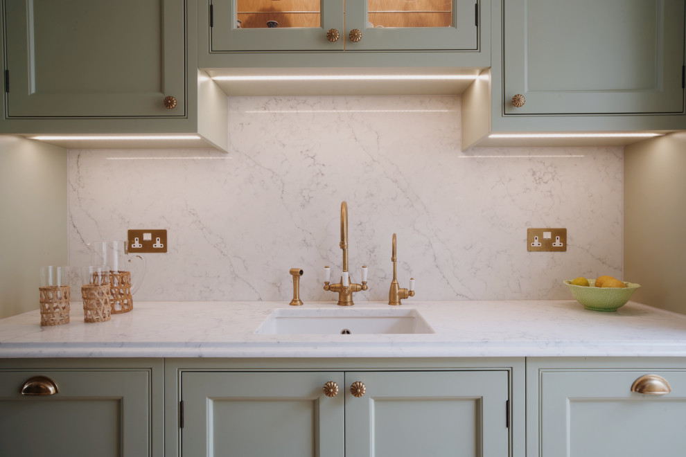 Small traditional galley enclosed kitchen in London with a submerged sink, shaker cabinets, green cabinets, quartz worktops, white splashback, engineered quartz splashback, black appliances, light hardwood flooring, no island, beige floors and white worktops.