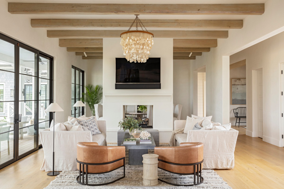 Inspiration for a coastal open plan living room in Charleston with white walls, light hardwood flooring, a two-sided fireplace, a plastered fireplace surround, a wall mounted tv and exposed beams.