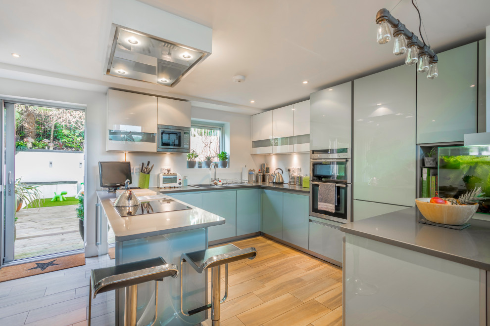 Inspiration for a mid-sized contemporary u-shaped kitchen in Sussex with a drop-in sink, flat-panel cabinets, blue cabinets, stainless steel appliances, beige floor and grey benchtop.