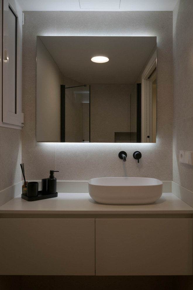 На фото: ванная комната среднего размера в стиле модернизм с белыми фасадами, душевой комнатой, унитазом-моноблоком, бежевой плиткой, бежевыми стенами, душевой кабиной, настольной раковиной, столешницей из искусственного камня, бежевым полом, душем с распашными дверями, бежевой столешницей, зеркалом с подсветкой и тумбой под одну раковину