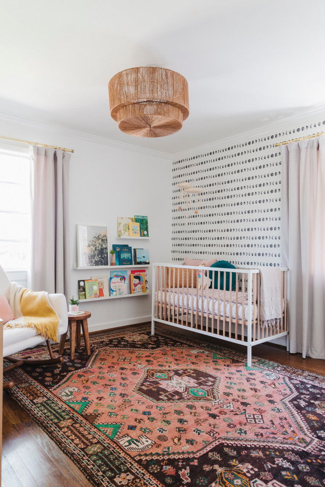 Imagen de habitación de bebé niña actual de tamaño medio con paredes blancas, suelo de madera en tonos medios y papel pintado