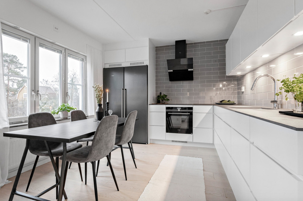 This is an example of a mid-sized scandinavian l-shaped eat-in kitchen in Stockholm with a single-bowl sink, flat-panel cabinets, white cabinets, laminate benchtops, grey splashback, porcelain splashback, stainless steel appliances, grey benchtop, no island and beige floor.