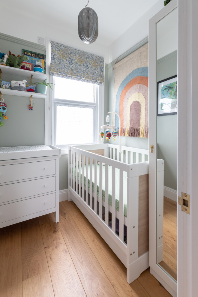 Immagine di una piccola cameretta per neonato minimal con pareti verdi, pavimento in legno massello medio e pavimento marrone