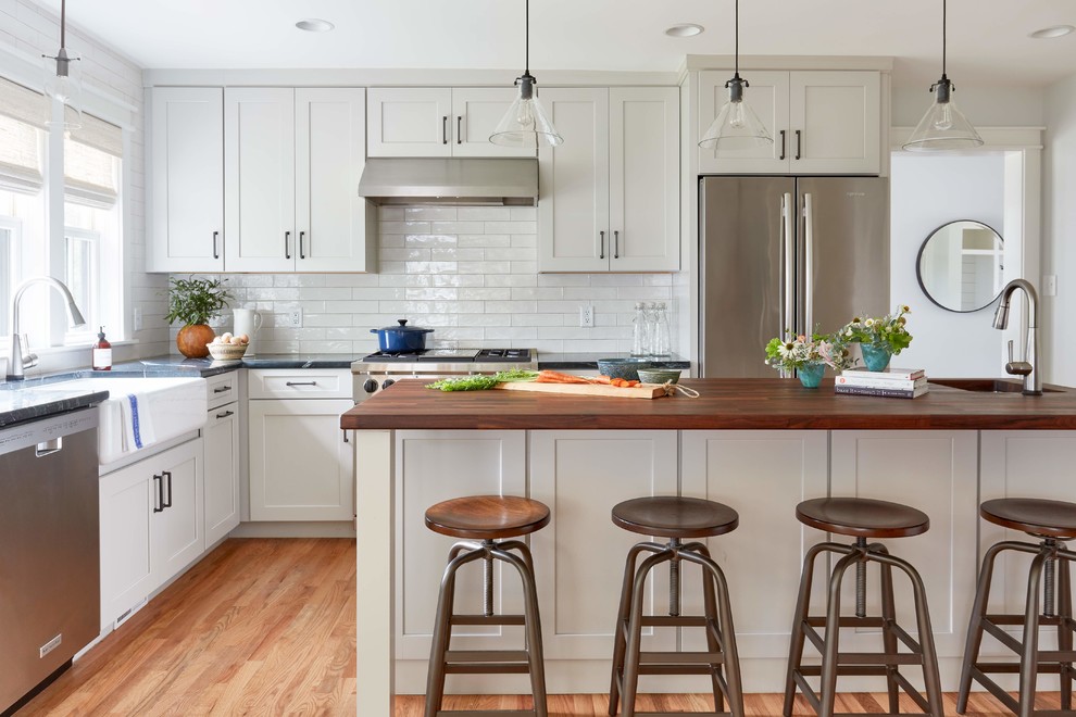Rockville - Inspiration for a large farmhouse l-shaped medium tone wood floor and brown floor kitchen remodel in Richmond with a farmhouse sink, shaker cabinets, white cabinets, wood countertops, white backsplash, subway tile backsplash, stainless steel appliances, an island and brown countertops