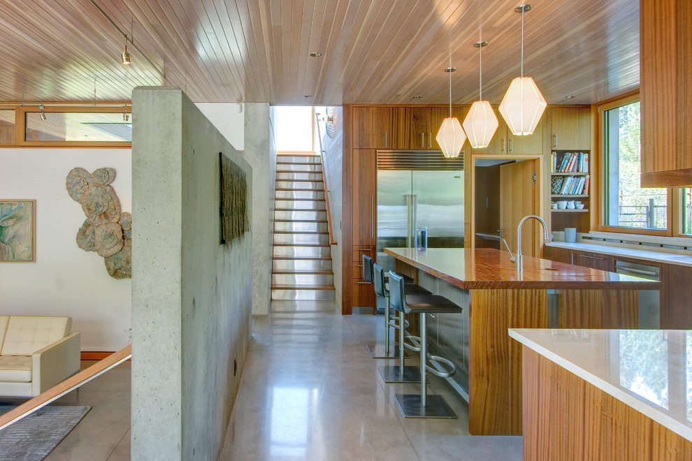 This is an example of a mid-sized contemporary u-shaped kitchen in Seattle with flat-panel cabinets, medium wood cabinets, solid surface benchtops, stainless steel appliances, concrete floors and with island.