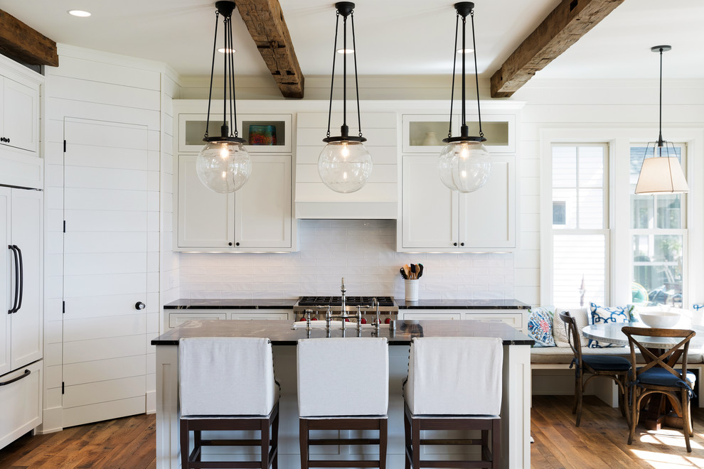 This is an example of a large beach style eat-in kitchen in Minneapolis with a farmhouse sink, shaker cabinets, white cabinets, granite benchtops, white splashback, subway tile splashback, panelled appliances, with island, brown floor and dark hardwood floors.
