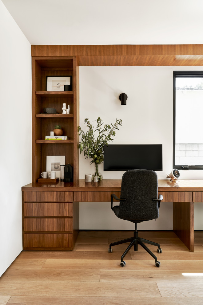 Idéer för mellanstora funkis hemmabibliotek, med vita väggar, mellanmörkt trägolv, ett inbyggt skrivbord och brunt golv
