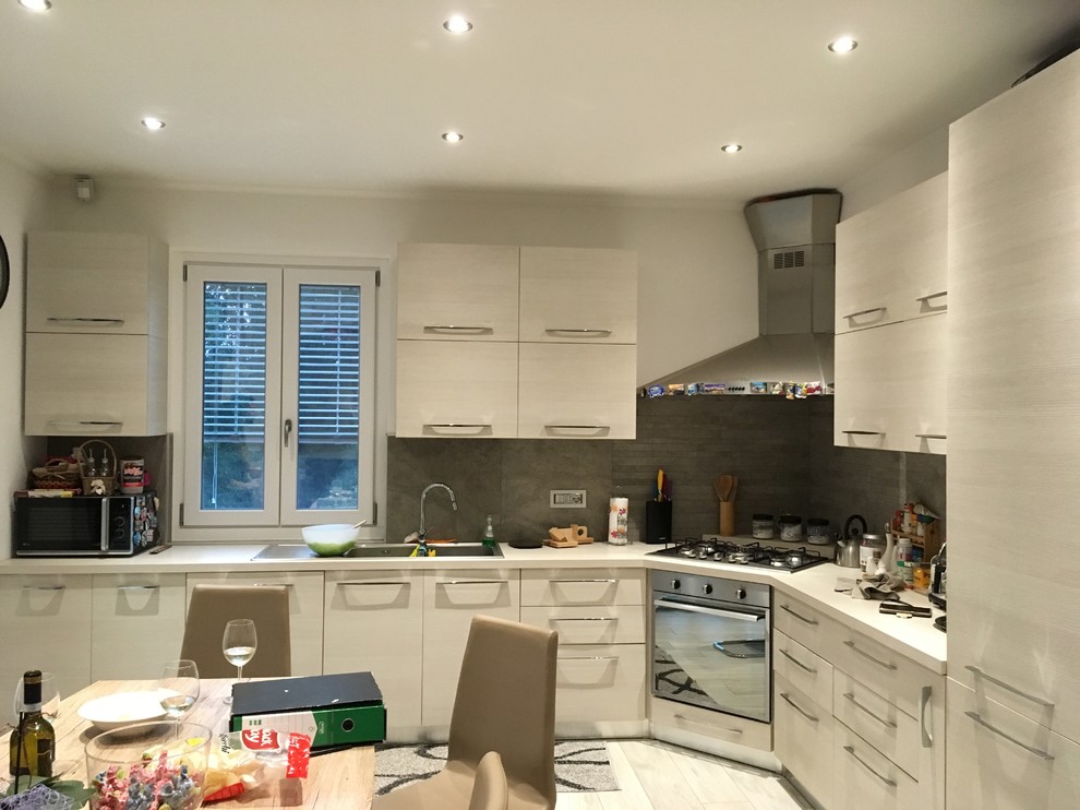 This is an example of a mid-sized contemporary l-shaped eat-in kitchen in Other with a double-bowl sink, flat-panel cabinets, beige cabinets, quartz benchtops, grey splashback, porcelain splashback, stainless steel appliances, light hardwood floors, no island, beige floor and beige benchtop.