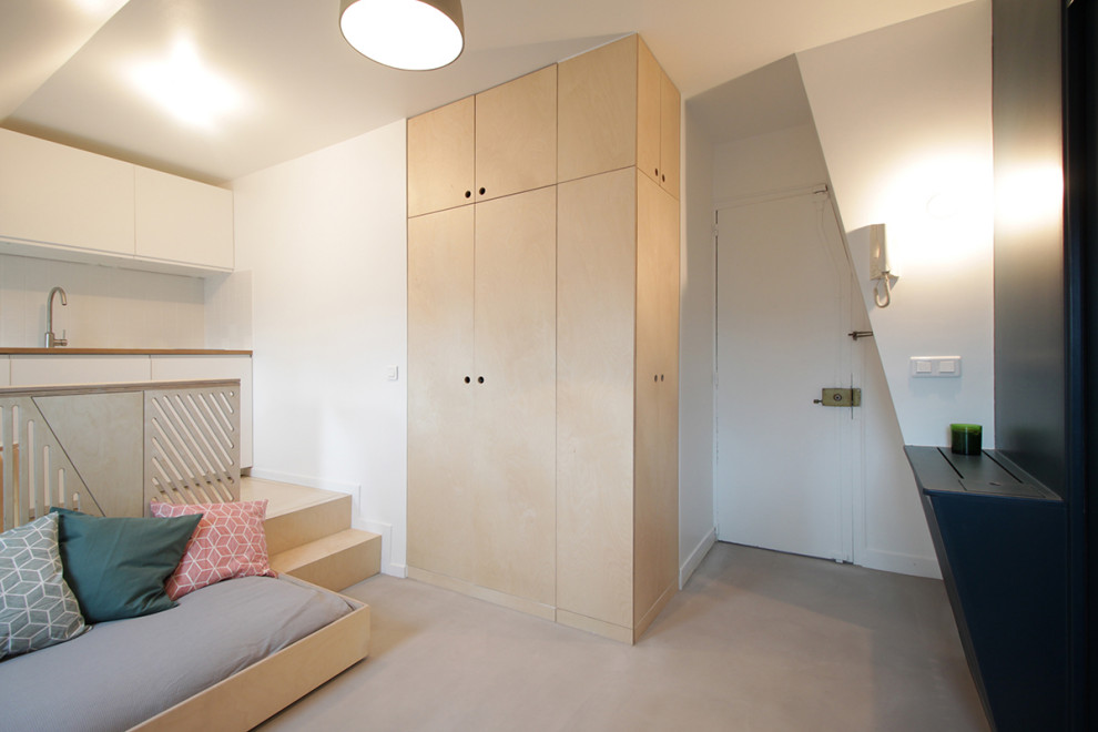 Réalisation d'une petite armoire encastrée design en bois clair neutre avec un placard à porte affleurante, sol en béton ciré et un sol gris.