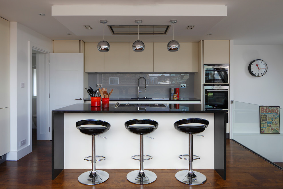 Design ideas for a large contemporary l-shaped open plan kitchen in London with flat-panel cabinets, grey splashback, with island, an integrated sink, white cabinets, granite benchtops, glass sheet splashback, panelled appliances, medium hardwood floors, brown floor and black benchtop.