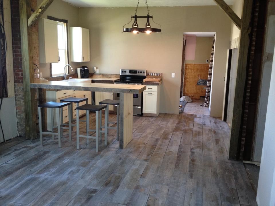 Inspiration for a mid-sized country l-shaped eat-in kitchen in Indianapolis with a farmhouse sink, beaded inset cabinets, white cabinets, wood benchtops, brown splashback, stainless steel appliances, ceramic floors and a peninsula.