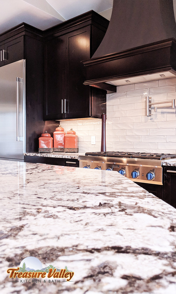 Inspiration for a mid-sized transitional l-shaped light wood floor open concept kitchen remodel in Boise with a farmhouse sink, shaker cabinets, granite countertops, glass tile backsplash, stainless steel appliances and an island