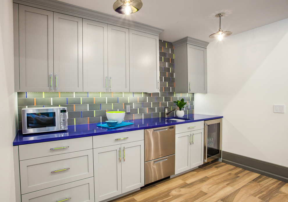 Photo of a mid-sized contemporary single-wall wet bar in Grand Rapids with an undermount sink, shaker cabinets, grey cabinets, solid surface benchtops, multi-coloured splashback, ceramic splashback, porcelain floors, brown floor and blue benchtop.
