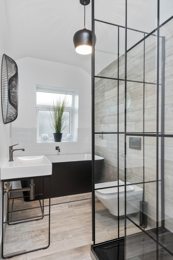 This is an example of a mid-sized industrial master bathroom in West Midlands with a freestanding tub, an open shower, a wall-mount toilet, white tile, beige walls, porcelain floors, a console sink, an open shower, subway tile and beige floor.