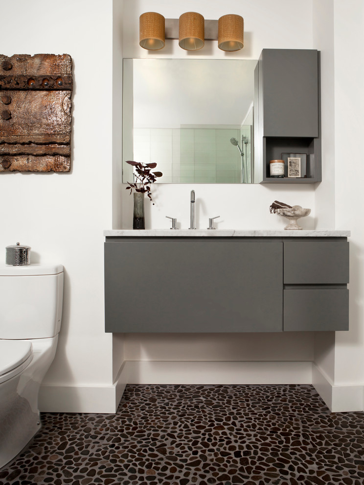 Mid-sized contemporary bathroom in Denver with white walls, pebble tile floors, a one-piece toilet, an undermount sink, flat-panel cabinets, grey cabinets, an alcove tub, a shower/bathtub combo, marble benchtops and white benchtops.
