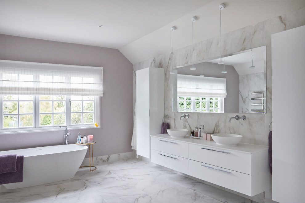 This is an example of a contemporary master bathroom in Surrey with flat-panel cabinets, white cabinets, a freestanding tub, marble, white walls, marble floors, a vessel sink, engineered quartz benchtops, grey floor, white benchtops, a double vanity and a floating vanity.