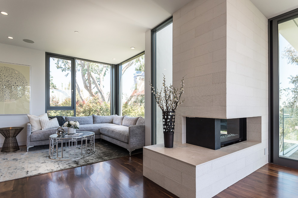 This is an example of a mid-sized modern master bedroom in Los Angeles with white walls, dark hardwood floors, a stone fireplace surround and a corner fireplace.