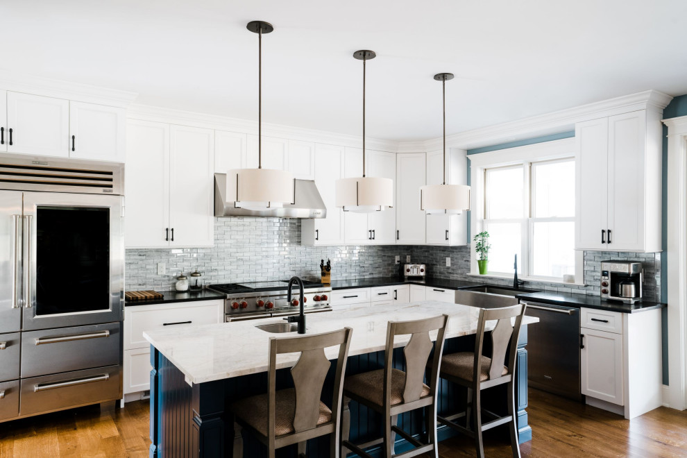 Large transitional l-shaped eat-in kitchen in Philadelphia with flat-panel cabinets, white cabinets, porcelain floors, brown floor, granite benchtops, grey splashback, glass tile splashback, stainless steel appliances, with island and black benchtop.