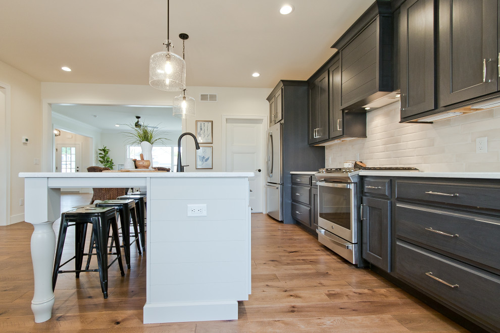Example of a transitional single-wall light wood floor and brown floor eat-in kitchen design with an undermount sink, raised-panel cabinets, dark wood cabinets, quartz countertops, white backsplash, brick backsplash, stainless steel appliances, an island and white countertops