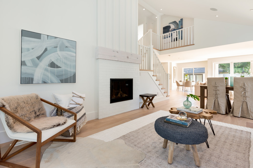 This is an example of a beach style open concept living room in Vancouver with white walls, light hardwood floors, a standard fireplace, a brick fireplace surround, no tv and beige floor.
