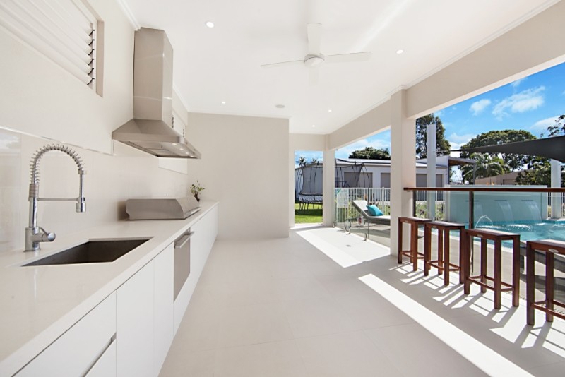 This is an example of a large tropical galley eat-in kitchen in Townsville with a drop-in sink, white cabinets, quartz benchtops, brown splashback, glass sheet splashback, stainless steel appliances, porcelain floors and with island.