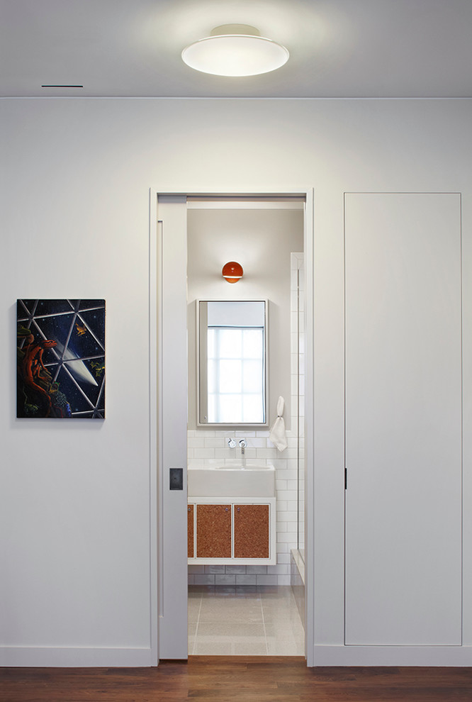 This is an example of a large modern bathroom in New York with a vessel sink, flat-panel cabinets, white cabinets, solid surface benchtops, an alcove shower, a one-piece toilet, white tile, ceramic tile and grey walls.