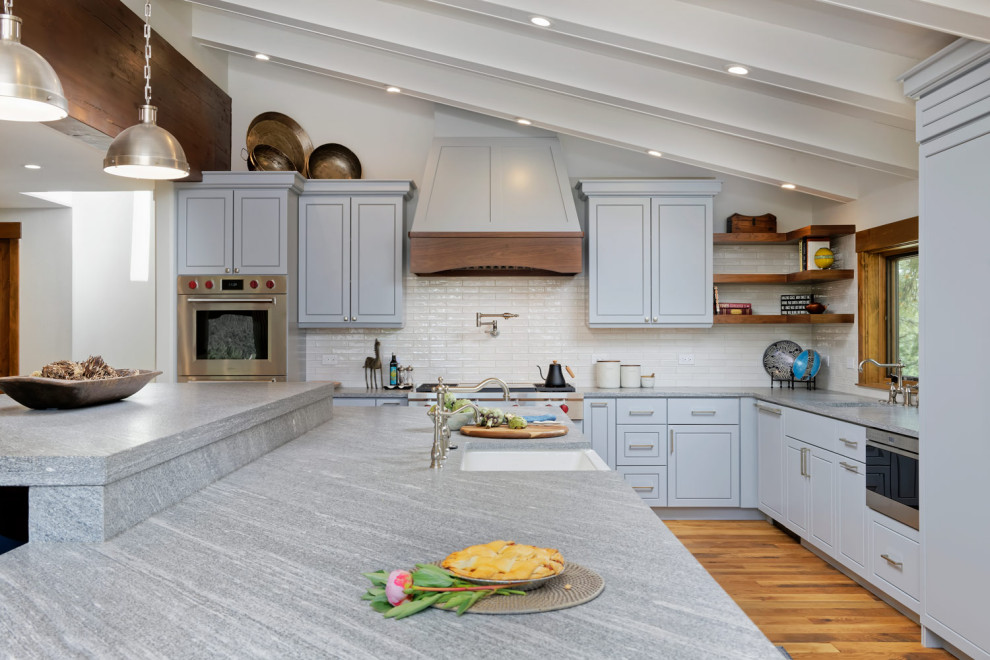 Mid-sized mountain style l-shaped medium tone wood floor open concept kitchen photo with an undermount sink, shaker cabinets, granite countertops, beige backsplash, stainless steel appliances and an island