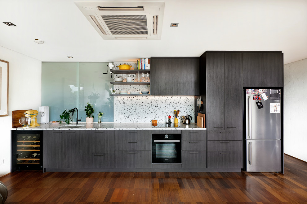 Design ideas for a large contemporary single-wall open plan kitchen in Melbourne with an undermount sink, flat-panel cabinets, brown cabinets, quartz benchtops, white splashback, stone tile splashback, black appliances, bamboo floors, no island, brown floor and white benchtop.